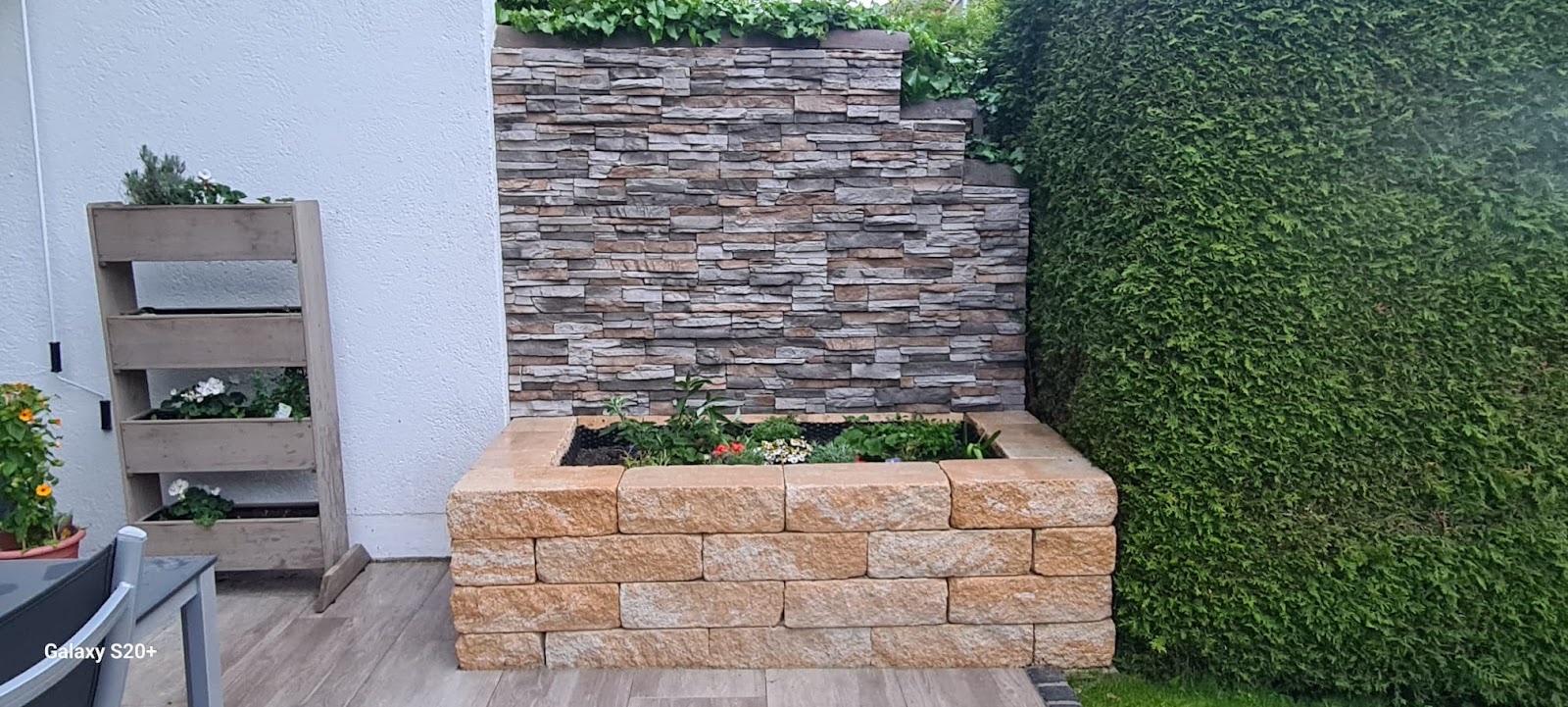 Hochbeet aus hellen Mauersteinen vor einer Wand aus Naturstein