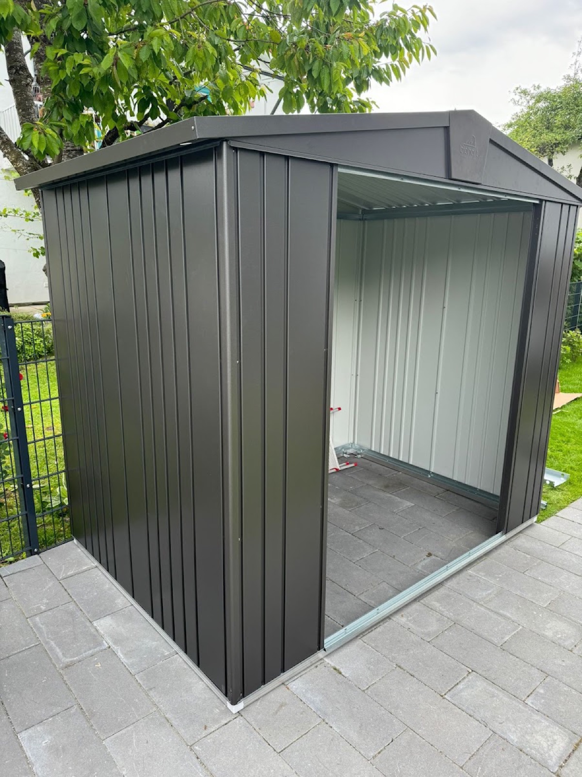 Anthrazitfarbenes Gerätehaus aus Metall auf gepflasterter Fläche